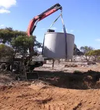 Crane lifting large concrete tank at construction site