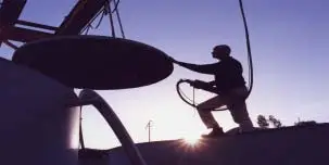 Silhouetted worker installing satellite dish at sunset