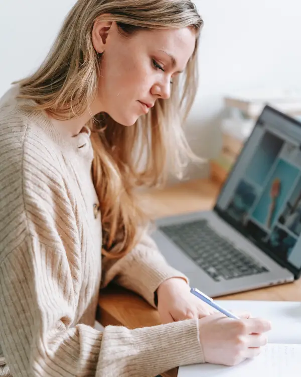 Woman writing notes at desk with laptop