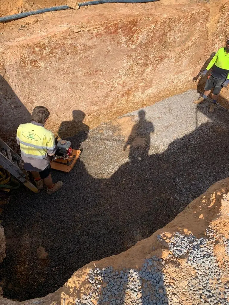 Workers compacting gravel in foundation excavation pit