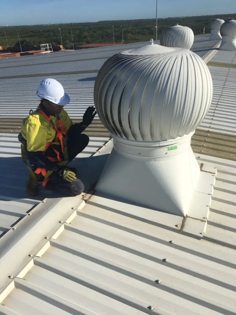 Worker inspecting roof turbine vent on metal roof